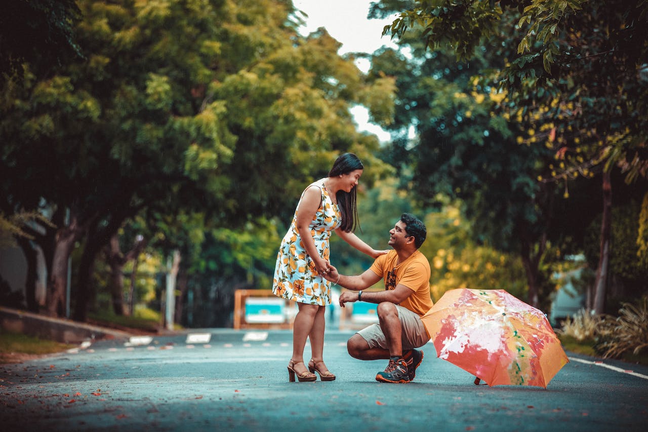 about-02 Man proposes to woman on a serene road amidst nature, creating a romantic and memorable moment.